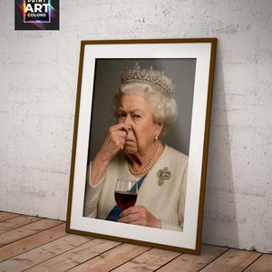May include: Framed print featuring a portrait of Queen Elizabeth II, wearing a crown and holding a glass of red wine. The image has a humorous expression. The frame is brown, and the print is leaning against a wall.