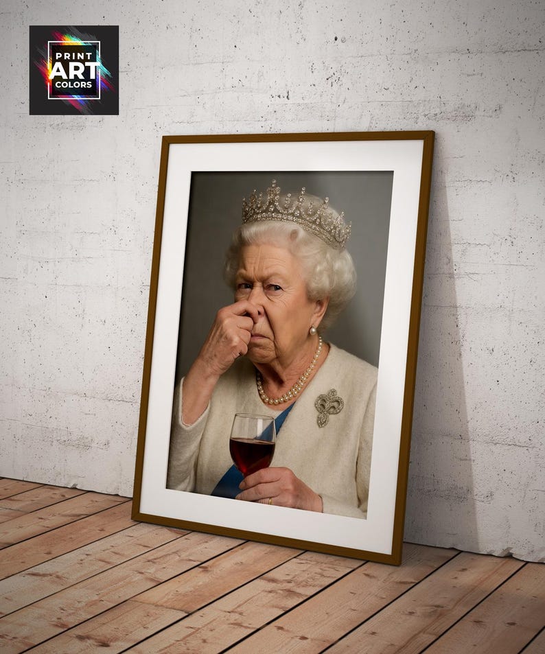 May include: Framed print featuring a portrait of Queen Elizabeth II, wearing a crown and holding a glass of red wine. The image has a humorous expression. The frame is brown, and the print is leaning against a wall.
