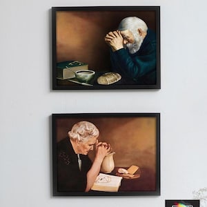 May include: Two framed wall art prints featuring realistic paintings of an elderly person praying at a table. The top print shows a man with a white beard, a book, a bowl, and bread. The bottom print shows a woman with white hair, a pitcher, and a book.