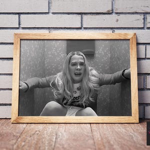 Puede incluir: Impresi&oacute;n enmarcada en blanco y negro de una mujer en una pose angustiada, sentada en un espacio peque&ntilde;o. La impresi&oacute;n est&aacute; en un marco de madera, colocada contra una pared de ladrillo y una superficie de madera. La imagen tiene una est&eacute;tica vintage.