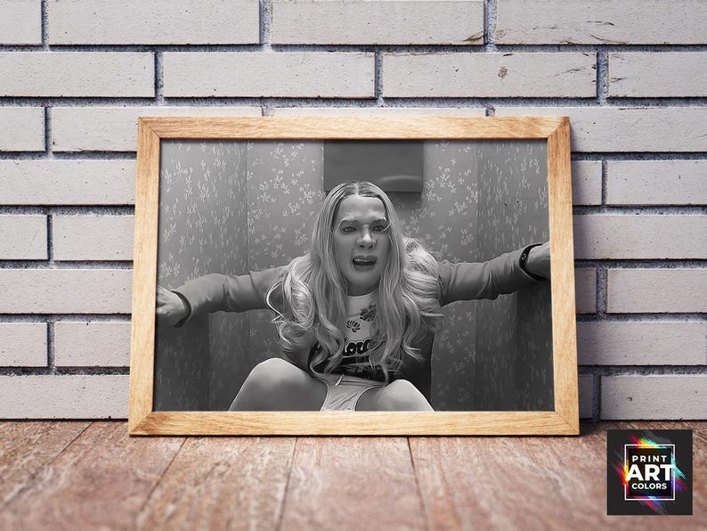 Puede incluir: Impresi&oacute;n enmarcada en blanco y negro de una mujer en una pose angustiada, sentada en un espacio peque&ntilde;o. La impresi&oacute;n est&aacute; en un marco de madera, colocada contra una pared de ladrillo y una superficie de madera. La imagen tiene una est&eacute;tica vintage.