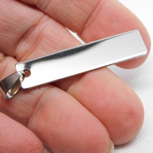 May include: A silver rectangular pendant with a smooth, polished surface and a jump ring for attaching to a chain.