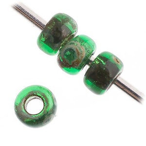 Puede incluir: Cuatro cuentas de vidrio verde con un patrón moteado. Las cuentas están enhebradas en un alambre plateado.