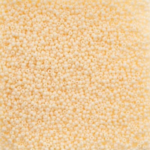 May include: A close-up shot of a pile of small, round, off-white beads. The beads are densely packed together, creating a textured surface. The color is a creamy, pale yellow, and the beads appear to be made of glass or a similar material. These beads are suitable for jewelry making and crafts.