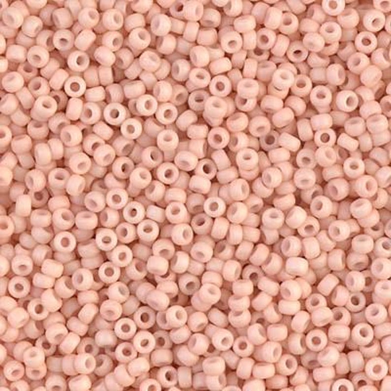 May include: A close-up view of a large quantity of small, round, light pink beads. The beads are opaque and have a smooth, slightly glossy finish.