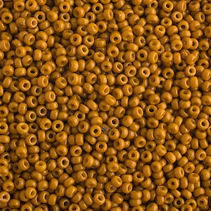 May include: A close-up image of a large quantity of small, round, opaque, golden brown beads. The beads are all the same size and shape, and they are arranged in a random pattern.