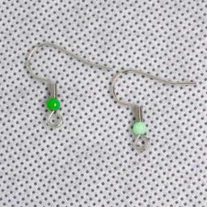 Op de afbeelding: Een paar zilveren oorhaken met groene kralen. De kralen zijn lichtgroen en donkergroen.