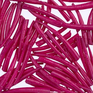 May include: A close-up shot of numerous, vibrant magenta-colored candy sticks. The sticks are arranged in a scattered pattern against a white background. The candy appears to be a chewy, cylindrical treat, possibly licorice or a similar confection.