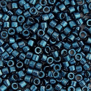May include: A close-up of numerous small, cylindrical beads. The beads are a deep teal colour with a metallic sheen, reflecting light. The beads are scattered, showing their tubular shape and open holes. These beads are suitable for jewellery making and crafts.