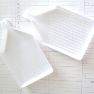 May include: Two white plastic diamond painting trays with ridges on the bottom. The trays are designed to hold diamonds for diamond painting.