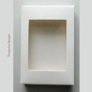 May include: A rectangular white box with a window cut out in the center. The text "Turquoise Opaque" is printed vertically on the left side of the box.