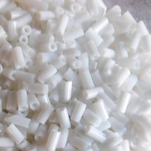 以下が含まれることがあります： 白い不透明なガラスビーズがたくさんあるクローズアップ画像。ビーズは小さく、円筒形です。