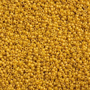 May include: Close-up of a pile of small, cylindrical, yellow seed beads. The beads are uniform in size and shape, with a hole running through the center of each. The beads are densely packed together, creating a textured surface. Ideal for jewelry making and crafts.
