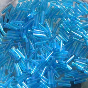May include: A large pile of iridescent blue glass beads. The beads are long and thin, resembling small tubes.