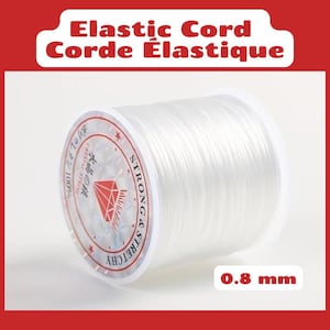 Peut inclure: Une bobine de cordon élastique transparent d'un diamètre de 0,8 mm. La bobine présente une étiquette avec le texte Elastic Cord, Corde Élastique, Strong & Stretchy et un motif de diamant. Le cordon est enroulé autour du cylindre en plastique.
