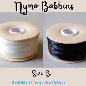 May include: Two spools of thread, one white and one black, on wooden bobbins. The bobbins are labeled "Nymo Bobbins" and "Size B".