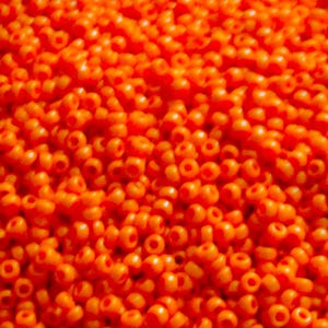 May include: A large collection of small, round, opaque orange seed beads. Each individual bead features a central hole and a smooth, uniform surface texture. The beads are densely packed together, creating a vibrant, monochromatic orange field.