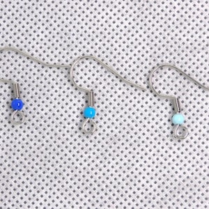 Op de afbeelding: Drie zilveren oorhaken met verschillende gekleurde kralen. De kralen zijn blauw, turquoise en lichtblauw.