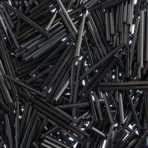 May include: A pile of black glass rods, also known as glass beads or glass strands, used for jewellery making and other craft projects.