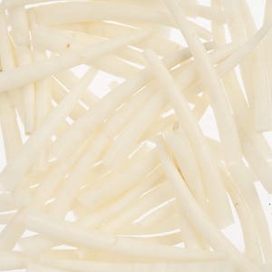 May include: A close-up shot showing a collection of white, thin, and gently curved items, possibly food. They are scattered in a random arrangement against a bright white backdrop. The image has a clean and minimalist aesthetic.