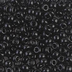 May include: A close-up shot of a pile of small, glossy black beads. Each bead has a rounded shape with a hole running through the center. The beads are densely packed together, creating a textured surface.