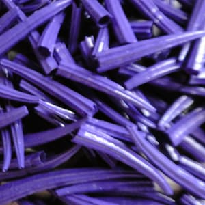 Peut inclure: Une collection de nombreuses petites pointes ou tubes creux en plastique violet. Chaque pièce présente une extrémité effilée et pointue ainsi qu'une base cylindrique ouverte. Les objets sont dispersés en un tas dense et chevauchant.