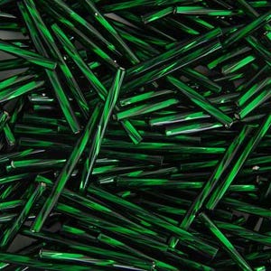 Peut inclure: Une collection de nombreuses perles tubes en verre, longues et fines, de couleur vert émeraude profond. Les perles présentent une surface lisse, réfléchissante et translucide qui capte la lumière, créant des reflets variés sur l'ensemble.