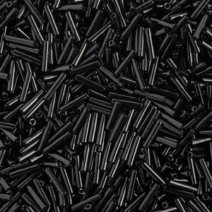 Peut inclure: Gros plan sur un tas de perles de rocaille en verre noir. Les perles sont cylindriques et brillantes. Elles sont dispersées au hasard, créant une surface texturée. Chaque perle mesure environ 0,2 cm de diamètre.