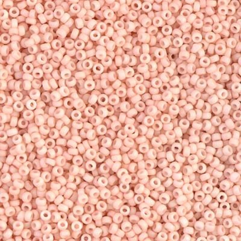 May include: A close-up image of a large quantity of small, round, light pink beads. The beads are opaque and have a smooth, glossy finish.