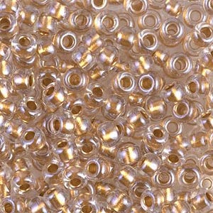 May include: A collection of small, round, transparent glass seed beads featuring a metallic gold-coloured core. Each bead has a smooth, glossy surface and a central hole, creating a uniform, reflective, and shimmering appearance across the group.