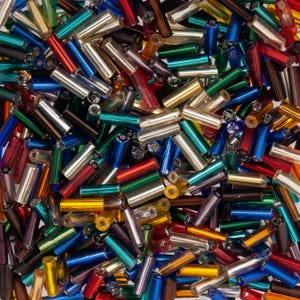 May include: A collection of small, cylindrical glass bugle beads in a vibrant assortment of metallic colours including red, blue, green, gold, silver, and bronze. Each bead features a smooth, reflective finish and a hollow centre for threading.