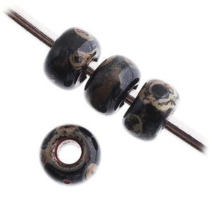 May include: Three round, glossy beads with a black base and mottled tan and brown patterns are threaded onto a silver-toned wire, while a fourth identical bead sits separately below, showing a clear centre hole and smooth, polished surface.