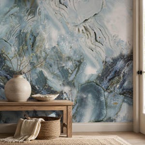 May include: A round ceramic vase and a woven basket containing a light-colored textile are placed on a wooden bench. The background features a wall mural with a blue and white marbled pattern resembling agate stone with swirling textures.
