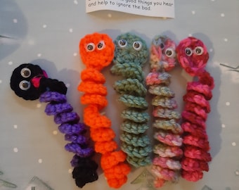 May include: Five crocheted colorful word worm toys with googly eyes. The worms are orange, green, pink, purple, and black. The worms are curled up and have a happy expression. The text on the card reads: "I'm your Happy Words Worm and I filter out the sads. I'll echo all the good things you hear and help to ignore the bad."