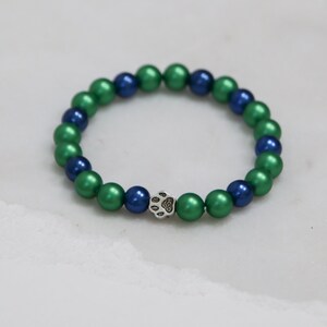 May include: A green and blue beaded bracelet with a silver paw print charm.
