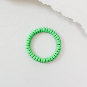 May include: A green silicone fidget ring with a circular shape. The ring is made of a series of small, connected beads.