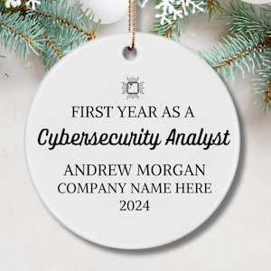 May include: White round Christmas ornament with black text that reads "First Year as a Cybersecurity Analyst", "Andrew Morgan", "Company Name Here", and "2024".