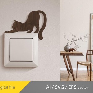 Op de afbeelding: Een houten katvormige lichtschakelaar in een rekpose, gemonteerd boven een witte lichtschakelaar. De kat is donkerbruin van kleur. De afbeelding bevat ook een tafel, stoel en decoratieve items.