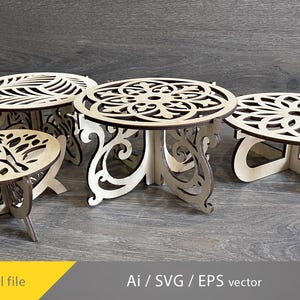 May include: Four decorative wooden stands with intricate, laser-cut designs. The stands feature circular tops with various patterns, including floral and tree motifs, supported by ornate, curved legs. The natural wood colour contrasts against the dark background.