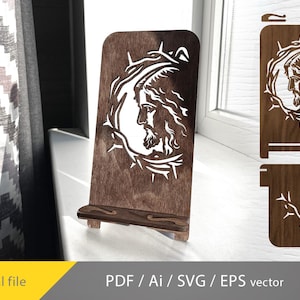 May include: A wooden phone stand with a laser cut design of a face surrounded by thorns. The stand is brown and has a small shelf for holding a phone.