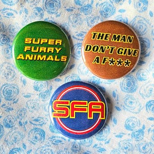 Super Furry Animals (indie / britpop / psych) three 25mm (1 inch) button pin badges including 'The Man Don't Give A F***' design.