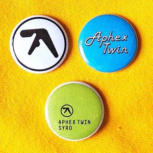 Aphex Twin (techno / electronnica) set of three 25mm (1 inch) button / pin badges with varying logo designs.