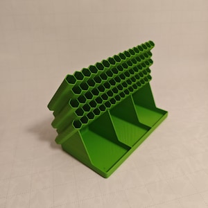 May include: A bright green, 3D-printed organizer with a honeycomb design. The organizer has multiple compartments and a tiered structure, ideal for storing small items. The base is rectangular, and the overall design is geometric.