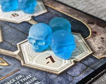 May include: A board game with blue translucent skull-shaped game pieces. The game board has a dark, textured design with white geometric shapes and numbers. The text on the board reads "ION" and other game instructions.