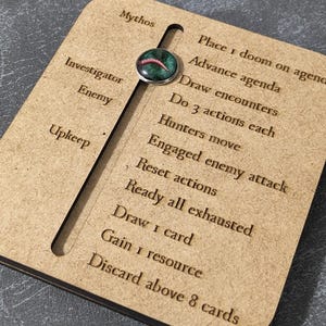 Könnte beinhalten: Ein Spiel-Tracker aus Holz mit einem Schieberegler und graviertem Text. Der Text enthält "Mythos", "Ermittler", "Feind" und "Instandhaltung". Der Tracker listet auch Spielaktionen wie "1 Karte ziehen" und "Über 8 Karten abwerfen".