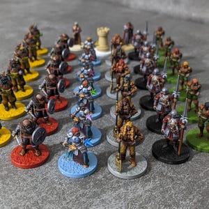 Puede incluir: Una colección de figuras de fantasía en miniatura, cada una pintada con armadura y armas detalladas. Las figuras se encuentran sobre bases circulares de colores, incluyendo amarillo, rojo, azul y verde. También hay una pequeña torre de castillo de color canela.