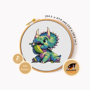 Pode incluir: Um padrão de ponto cruz num bastidor de madeira com um triceratops em estilo pixel art a comer uma folha verde. O design mede 24,1 x 27,4 cm. A imagem inclui etiquetas de texto para dificuldade, padrão PDF e a marca Jokahrt Cross Stitch.
