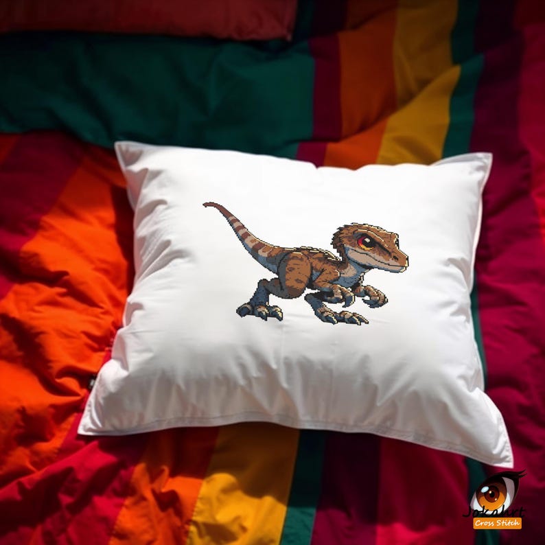 Pode incluir: Almofada quadrada branca com uma ilustra&ccedil;&atilde;o de desenho animado de um velociraptor marrom e bege com olhos vermelhos. A almofada est&aacute; em uma cama com um edredom listrado colorido.