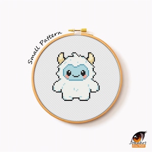 Puede incluir: Un patrón de punto de cruz de un lindo yeti de dibujos animados en un bastidor de bordado de madera. El yeti es blanco con una cara azul y pequeños cuernos. El texto "Small Pattern" está curvado.