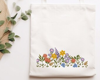 May include: A white canvas tote bag with a floral design. The flowers are in shades of yellow, orange, purple, and blue. The bag has two handles.